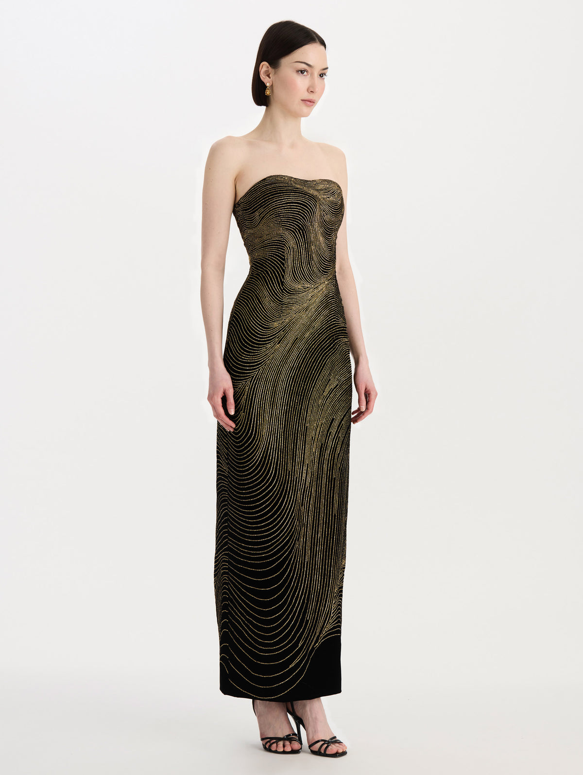 The model is wearing the beaded wave embroidered strapless cocktail dress in black and gold. Side view. 