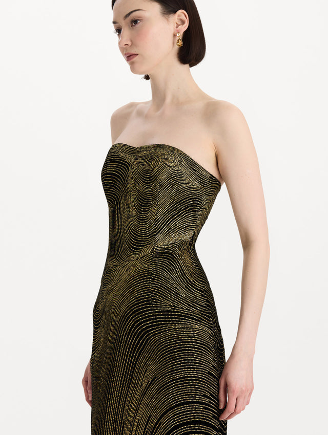 The model is wearing the beaded wave embroidered strapless cocktail dress in black and gold. Zoom view. 