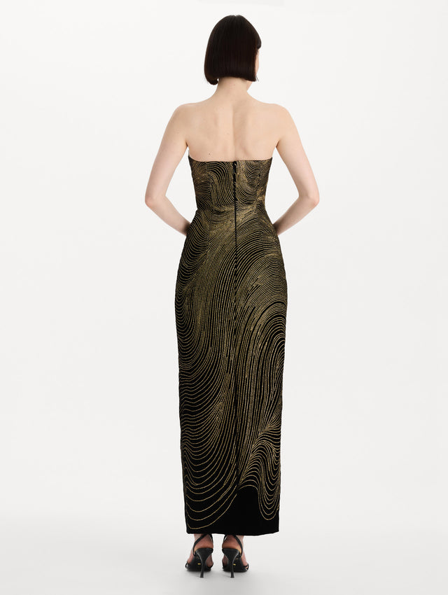 The model is wearing the beaded wave embroidered strapless cocktail dress in black and gold. Back view. 