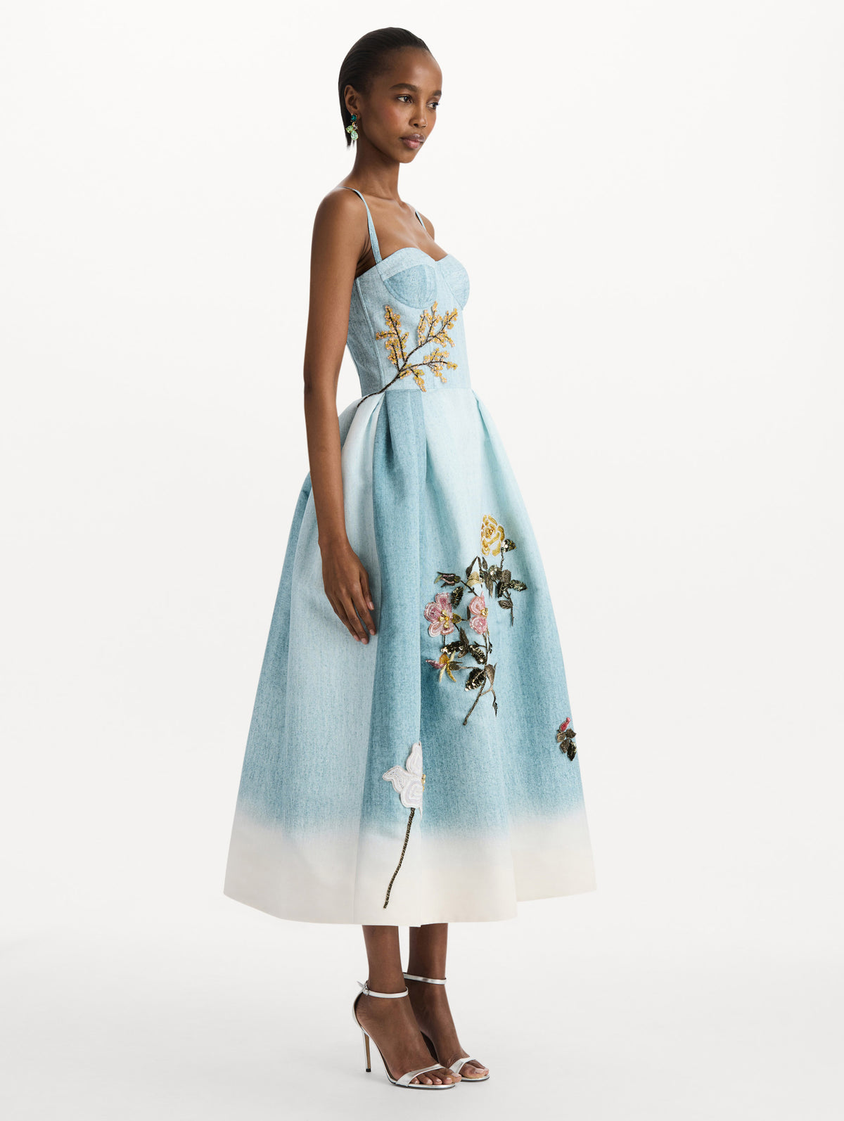 The model is wearing the beaded mixed botanical bustier dress with floral detailing and a sleeveless silhouette in blue multi. Side view. 