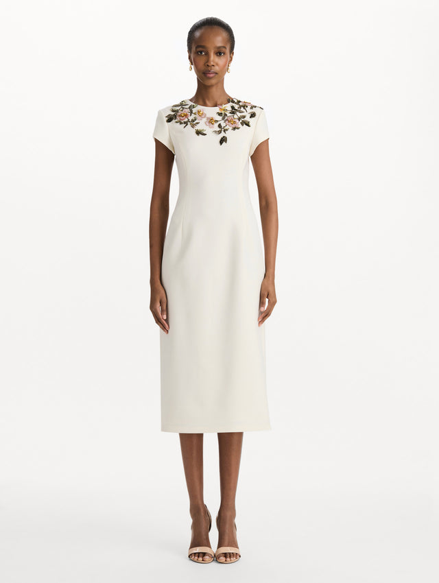 The model is wearing the beaded floral embroidered pencil dress with short sleeves in the color ivory. Front view. 