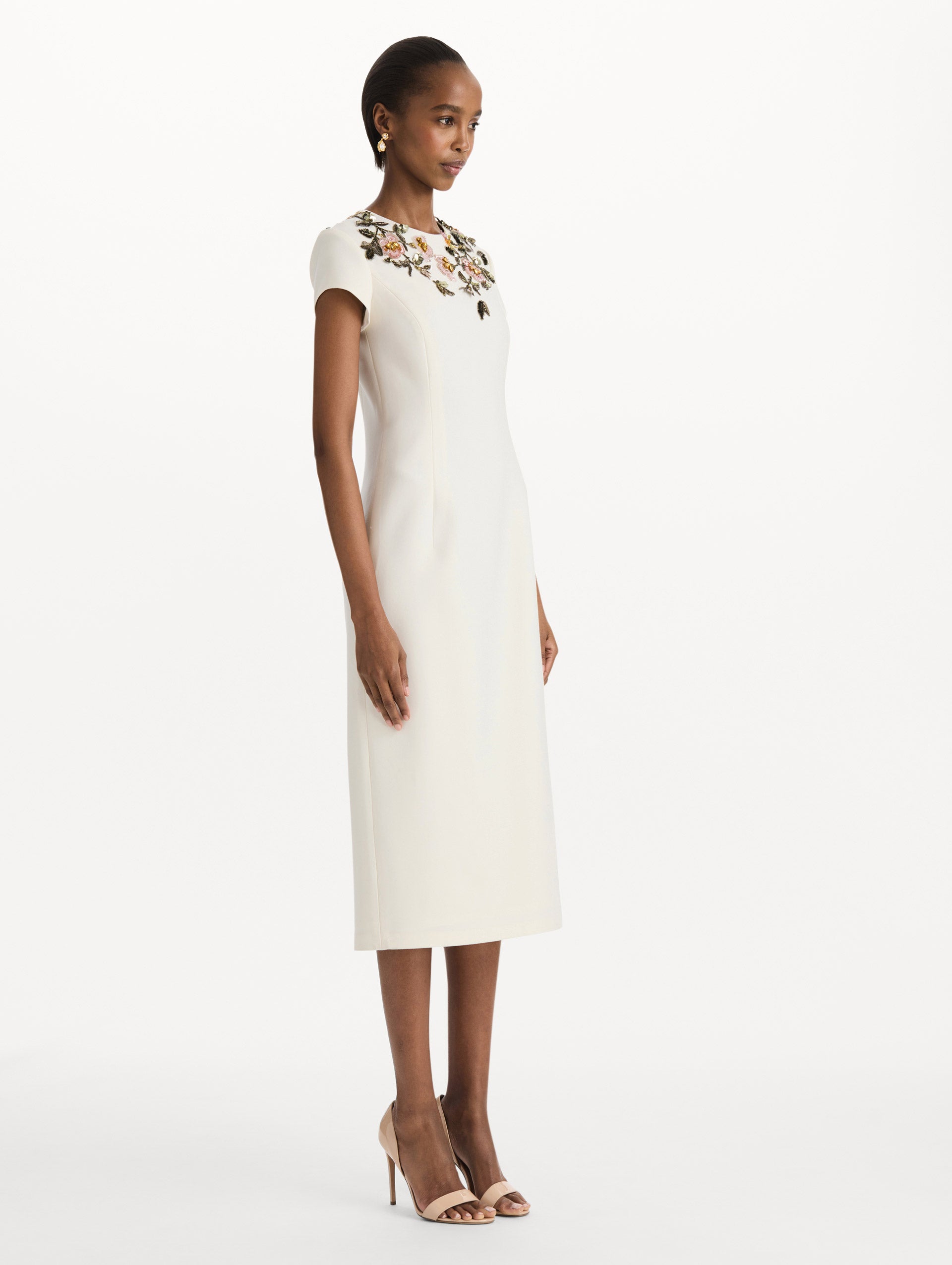 The model is wearing the beaded floral embroidered pencil dress with short sleeves in the color ivory. Side view. 