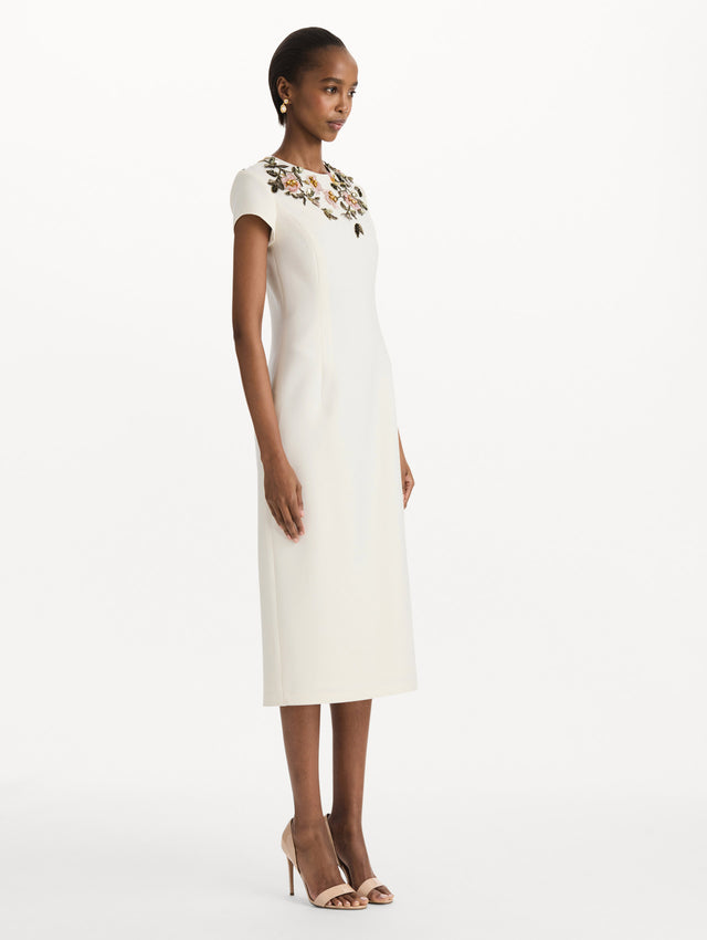 The model is wearing the beaded floral embroidered pencil dress with short sleeves in the color ivory. Side view. 