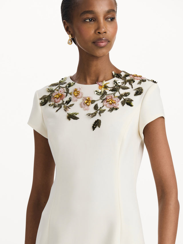 The model is wearing the beaded floral embroidered pencil dress with short sleeves in the color ivory. Zoom view. 