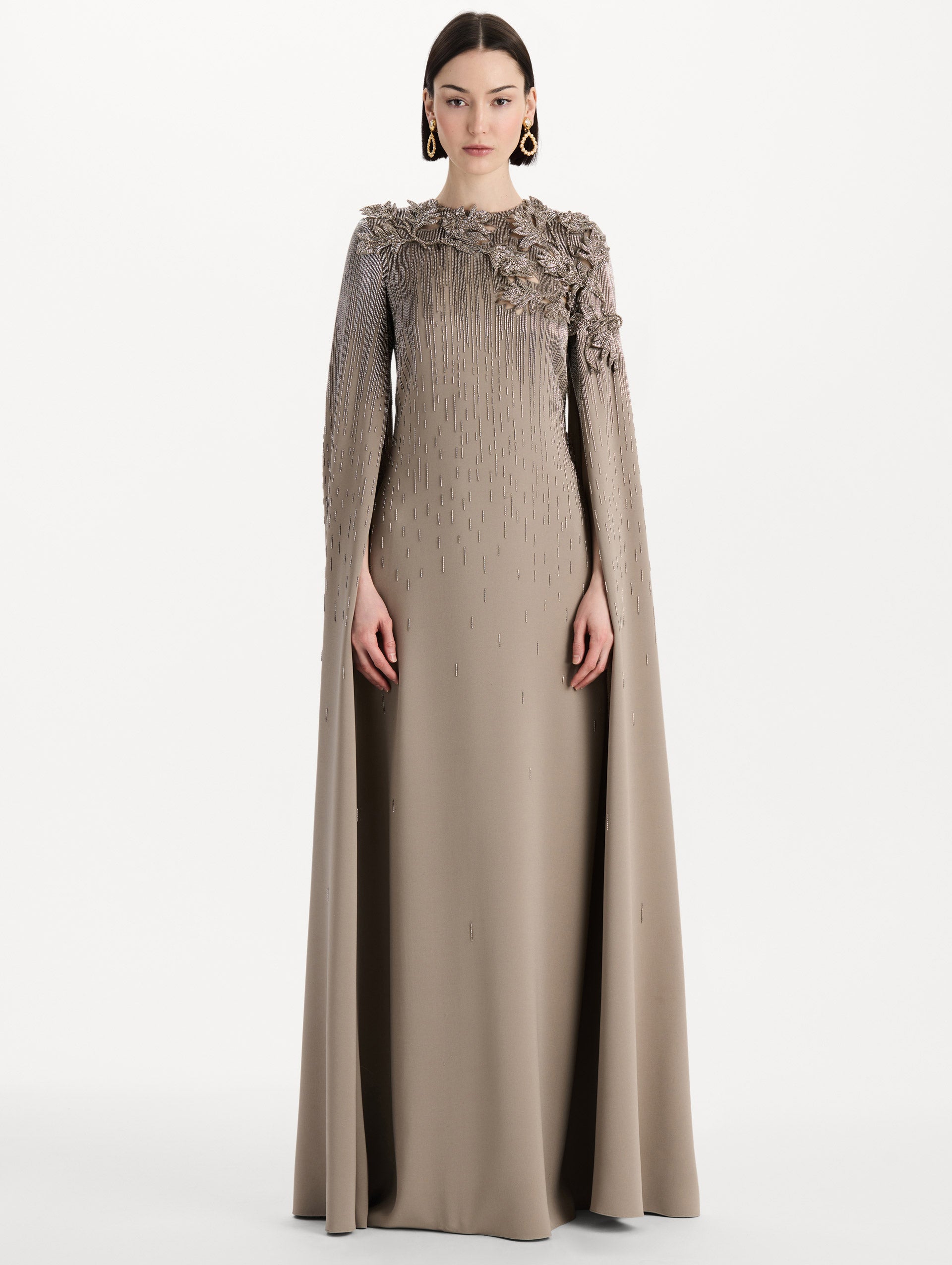 The model is wearing the intarsia leaves cutout embroidered caftan with long sleeves in the color stone. Front view. 