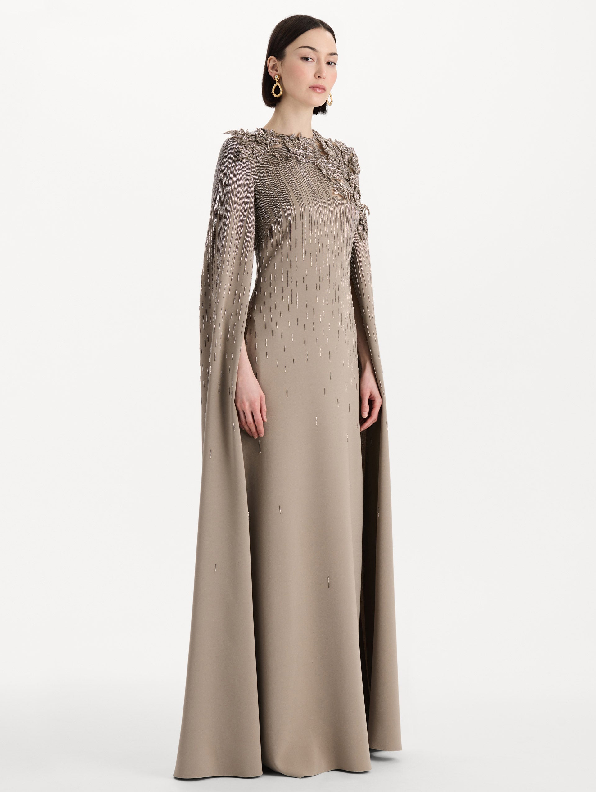 The model is wearing the intarsia leaves cutout embroidered caftan with long sleeves in the color stone. Side view.
