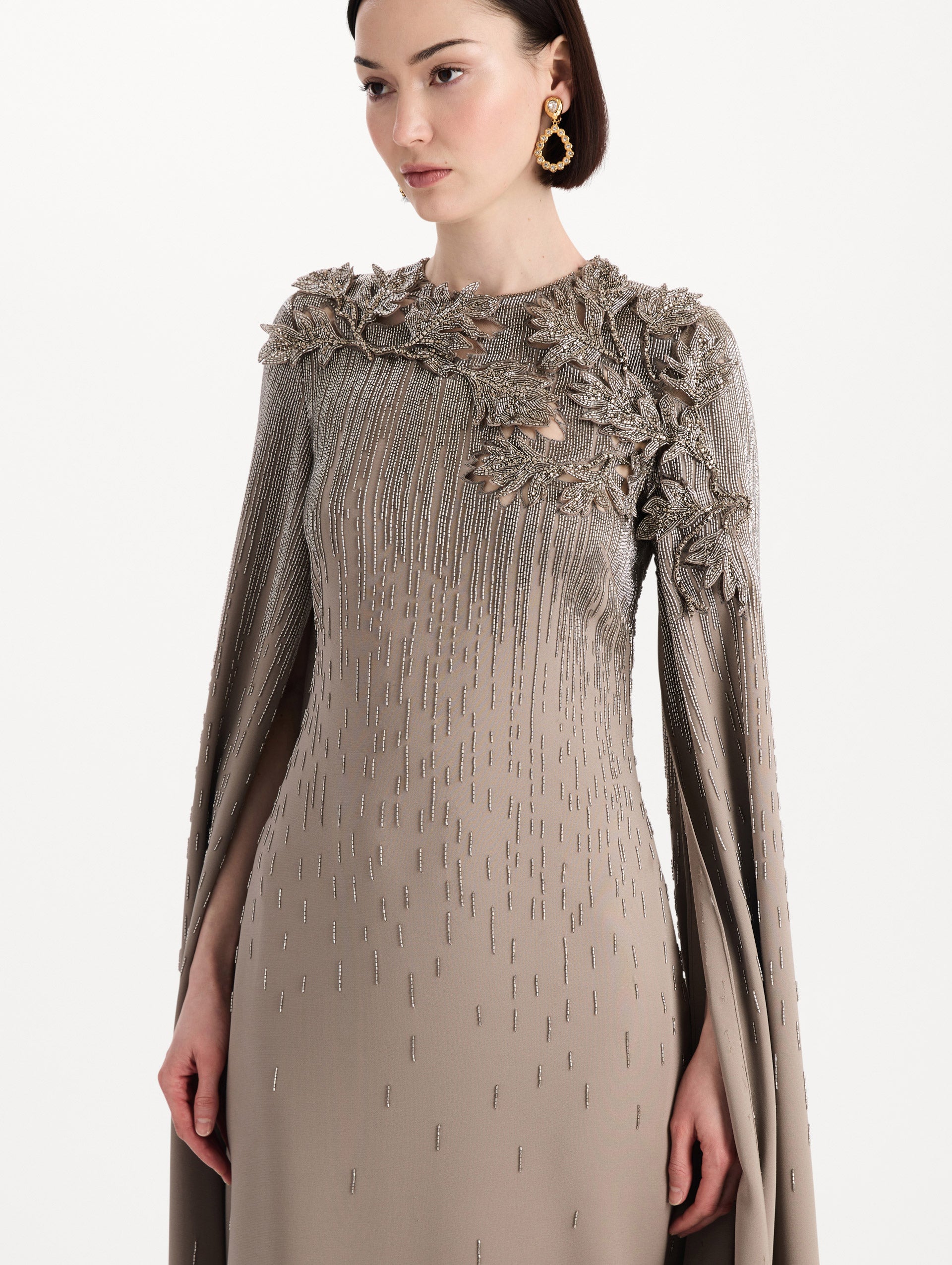 The model is wearing the intarsia leaves cutout embroidered caftan with long sleeves in the color stone. Zoom view.