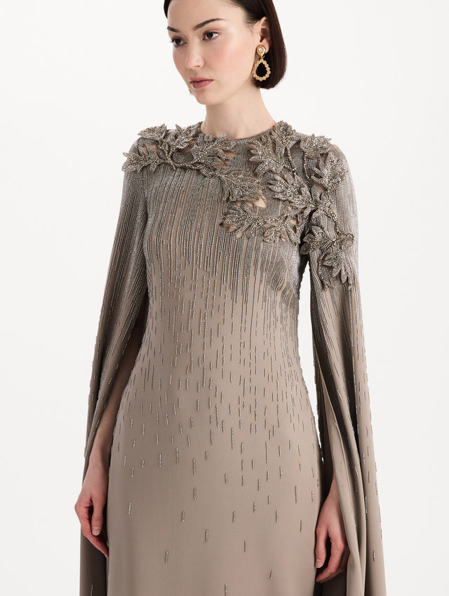 The model is wearing the intarsia leaves cutout embroidered caftan with long sleeves in the color stone. Zoom view.
