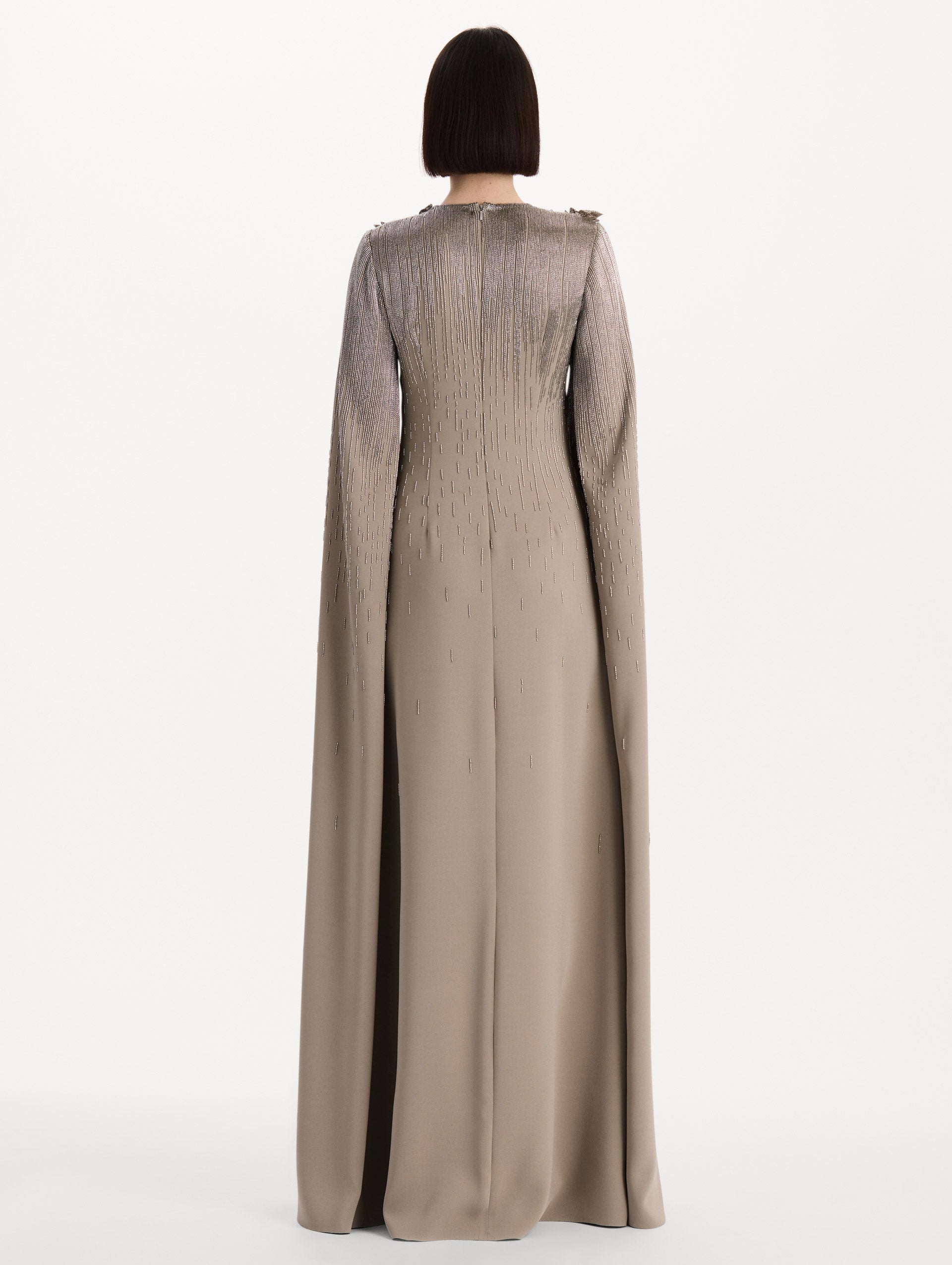 The model is wearing the intarsia leaves cutout embroidered caftan with long sleeves in the color stone. Back view. 