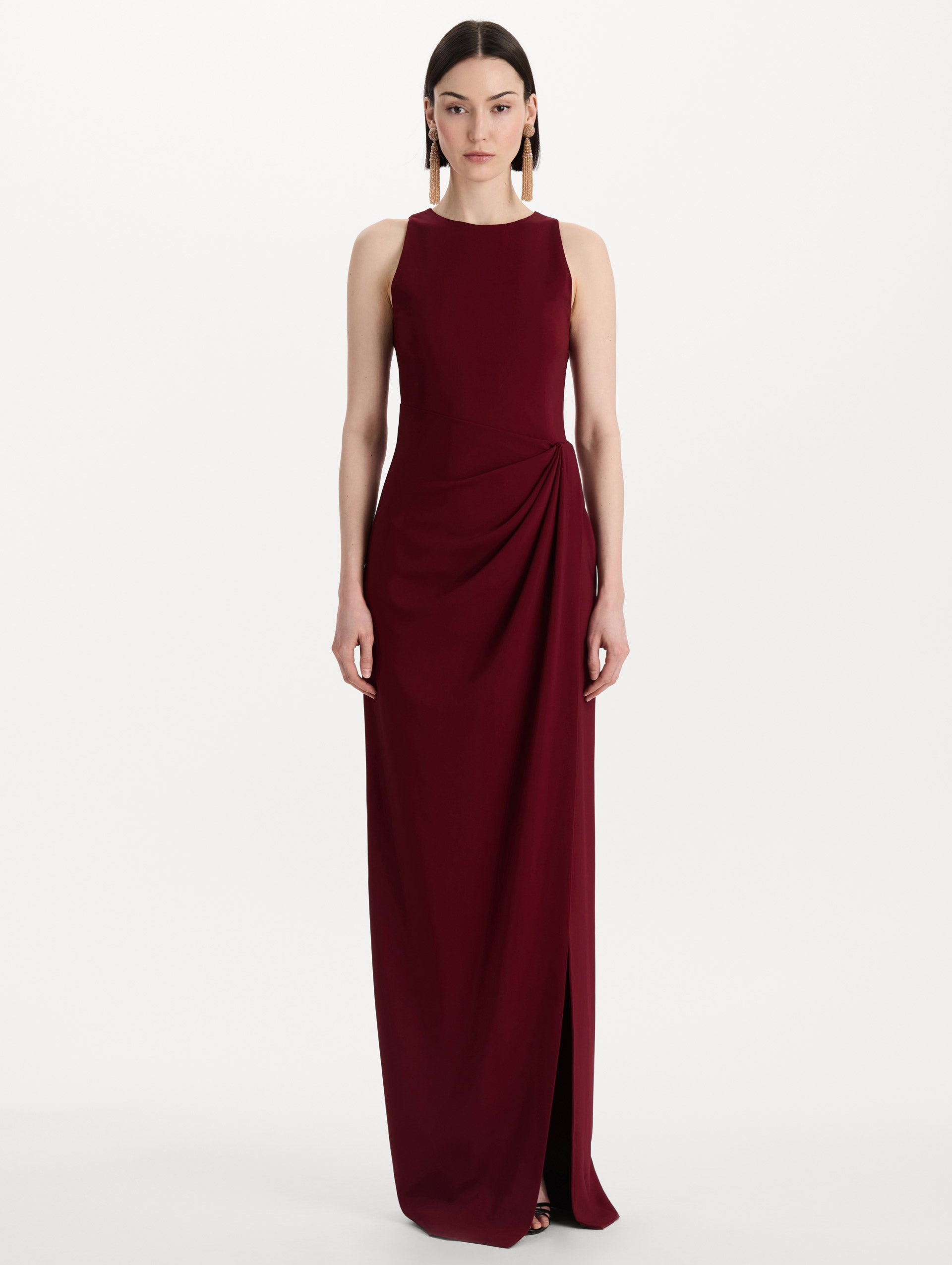 The model is wearing the drape-detailed cady gown with a sleeveless silhouette in the color claret. Front view. 
