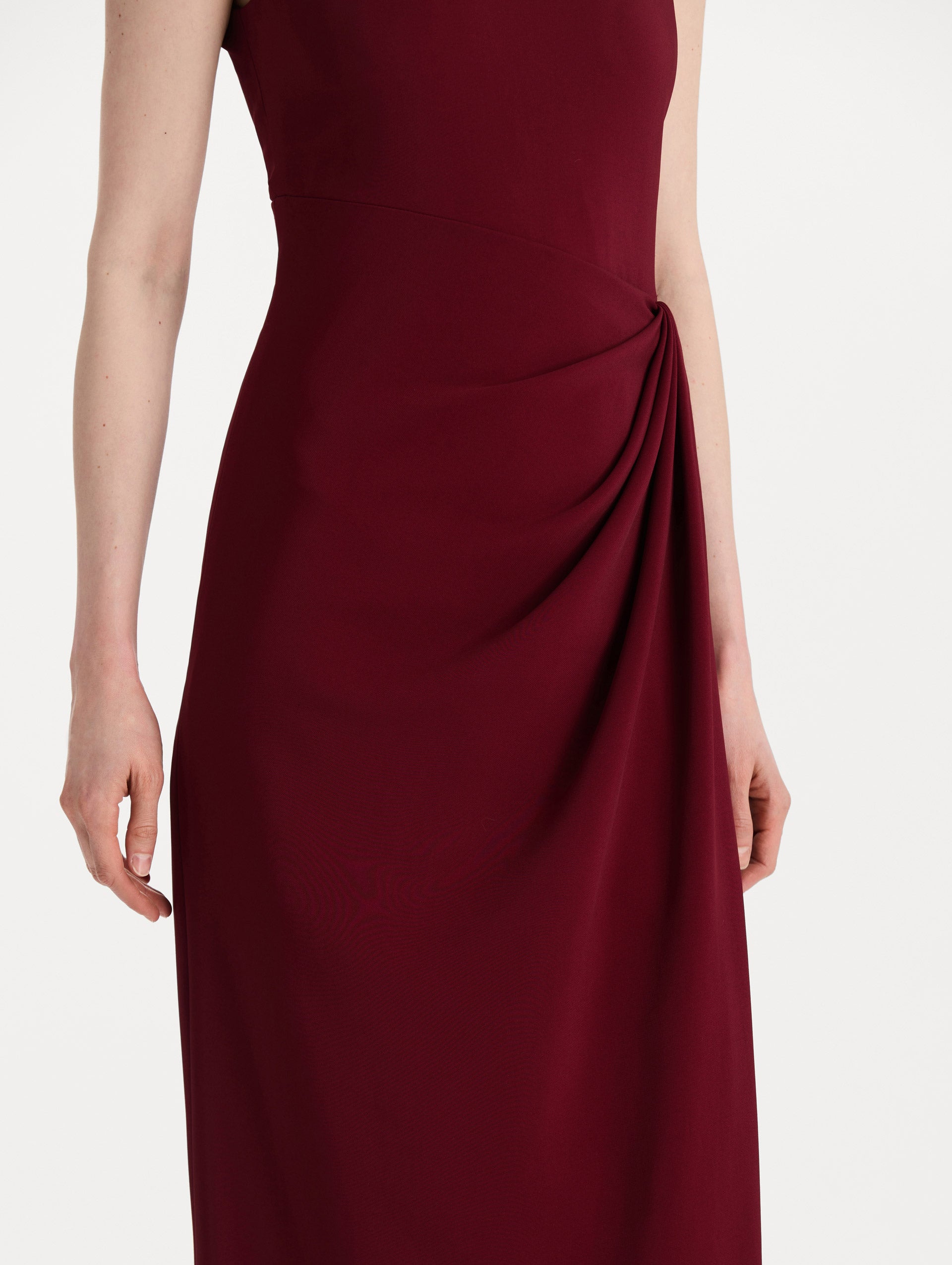The model is wearing the drape-detailed cady gown with a sleeveless silhouette in the color claret. Zoom view. 