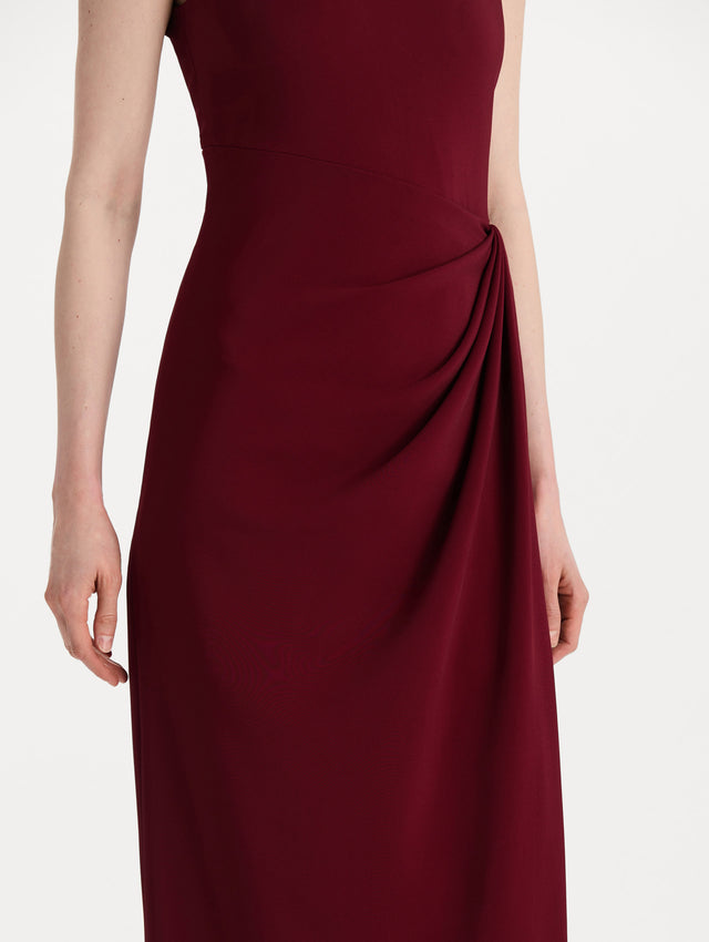 The model is wearing the drape-detailed cady gown with a sleeveless silhouette in the color claret. Zoom view. 