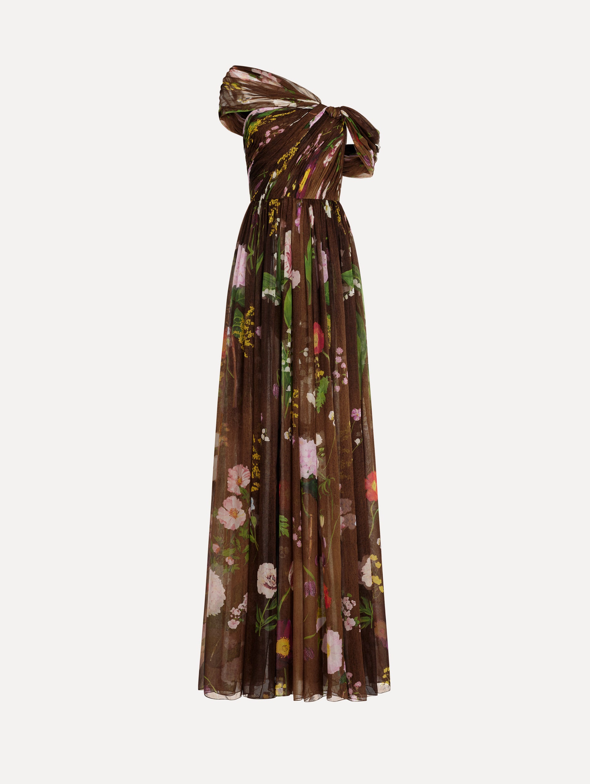 The model is wearing the mixed botanical silk chiffon gown with a one-shoulder neckline and a painterly floral print in a brown multi palette.