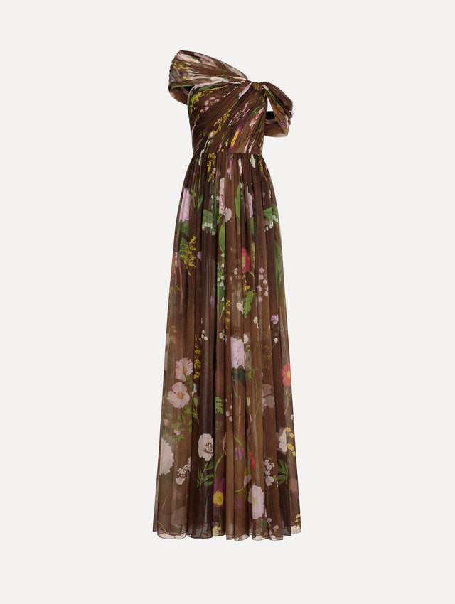 The model is wearing the mixed botanical silk chiffon gown with a one-shoulder neckline and a painterly floral print in a brown multi palette.