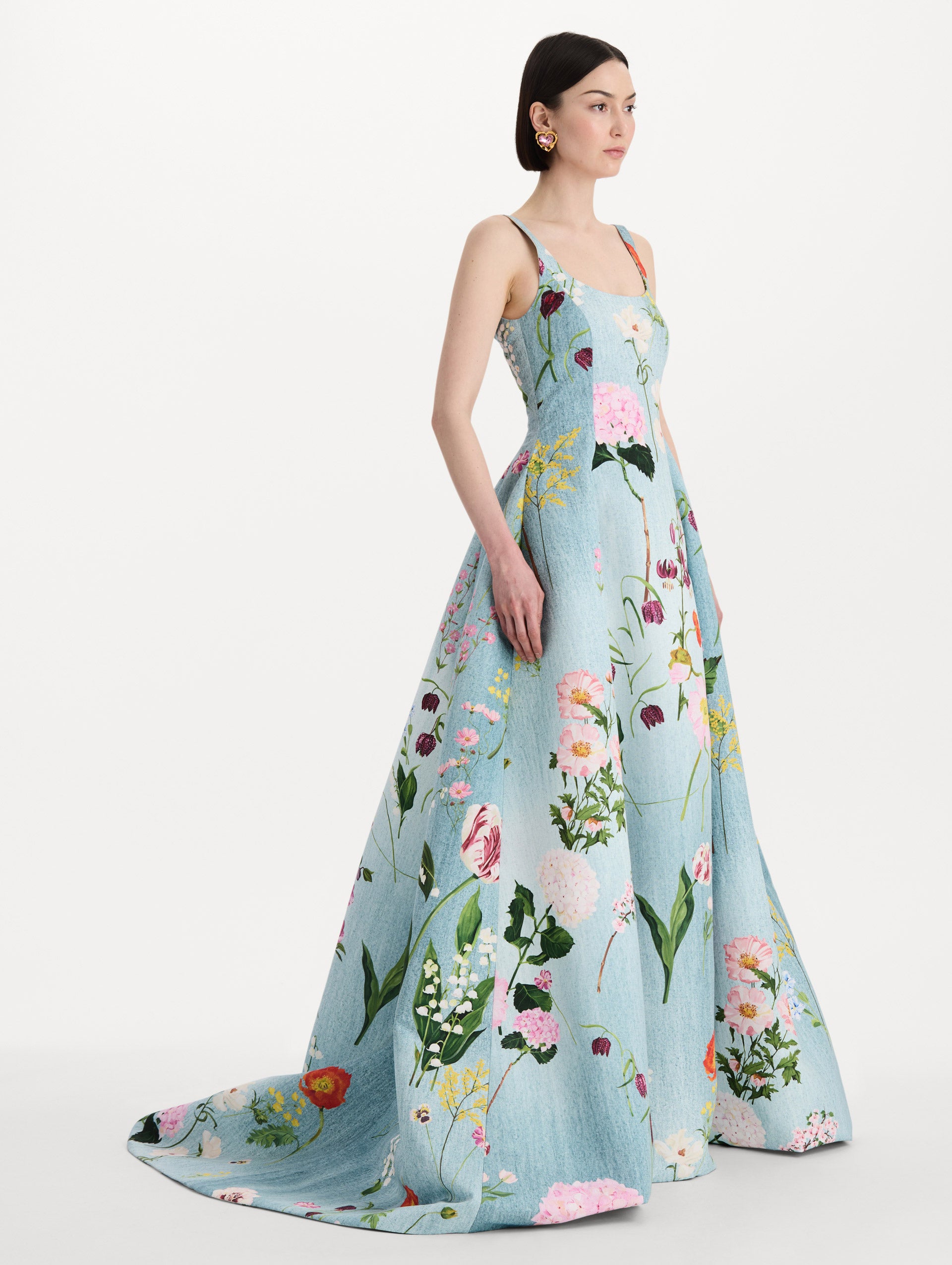 The model is wearing the mixed botanical faille gown with a sleeveless scoop neckline and a bold floral print in blue multi. Side view. 