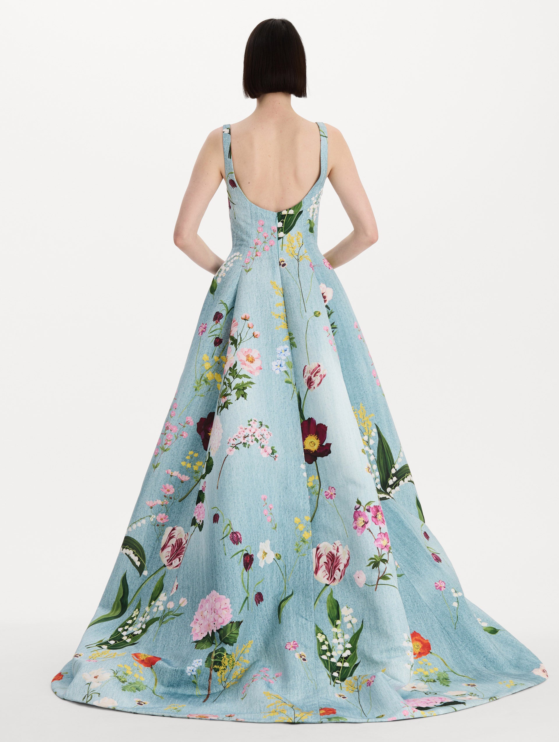 The model is wearing the mixed botanical faille gown with a sleeveless scoop neckline and a bold floral print in blue multi. Back view. 