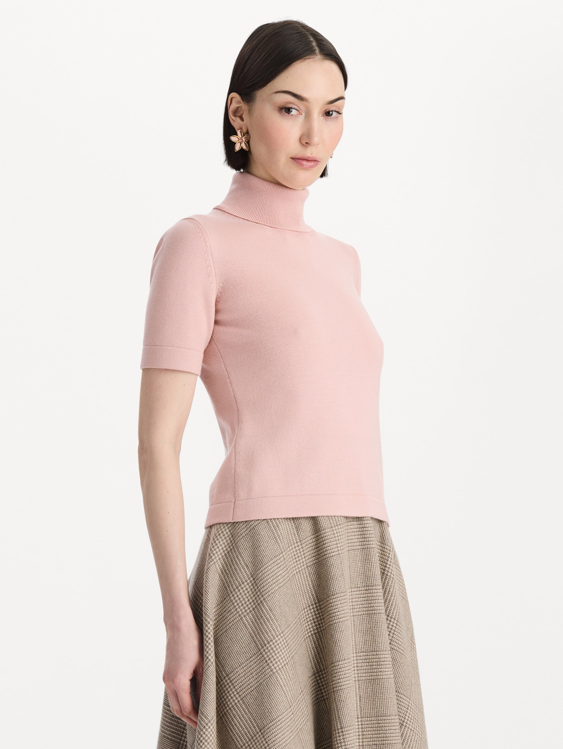 The model is wearing the turtleneck wool short-sleeve pullover with a fold-over neckline in the color blush. Side view.