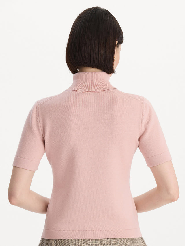 The model is wearing the turtleneck wool short-sleeve pullover with a fold-over neckline in the color blush. Back view.