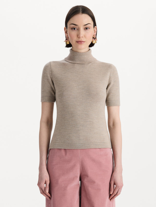 The model is wearing the turtleneck wool short-sleeve pullover with a fold-over neckline in the color dark oat. Front view. 
