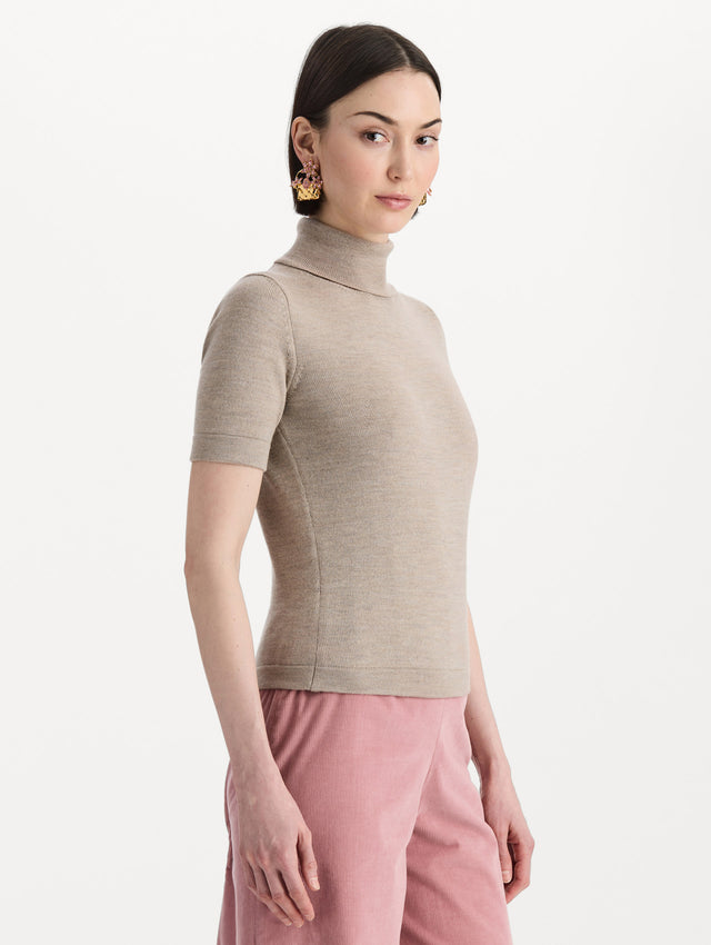 The model is wearing the turtleneck wool short-sleeve pullover with a fold-over neckline in the color dark oat. Side view. 