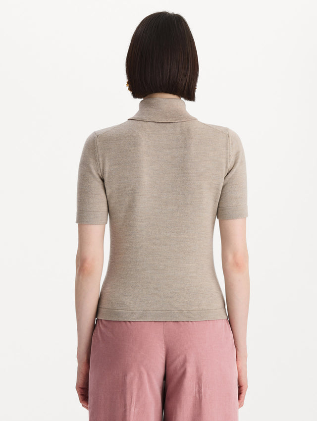 The model is wearing the turtleneck wool short-sleeve pullover with a fold-over neckline in the color dark oat. Back view. 