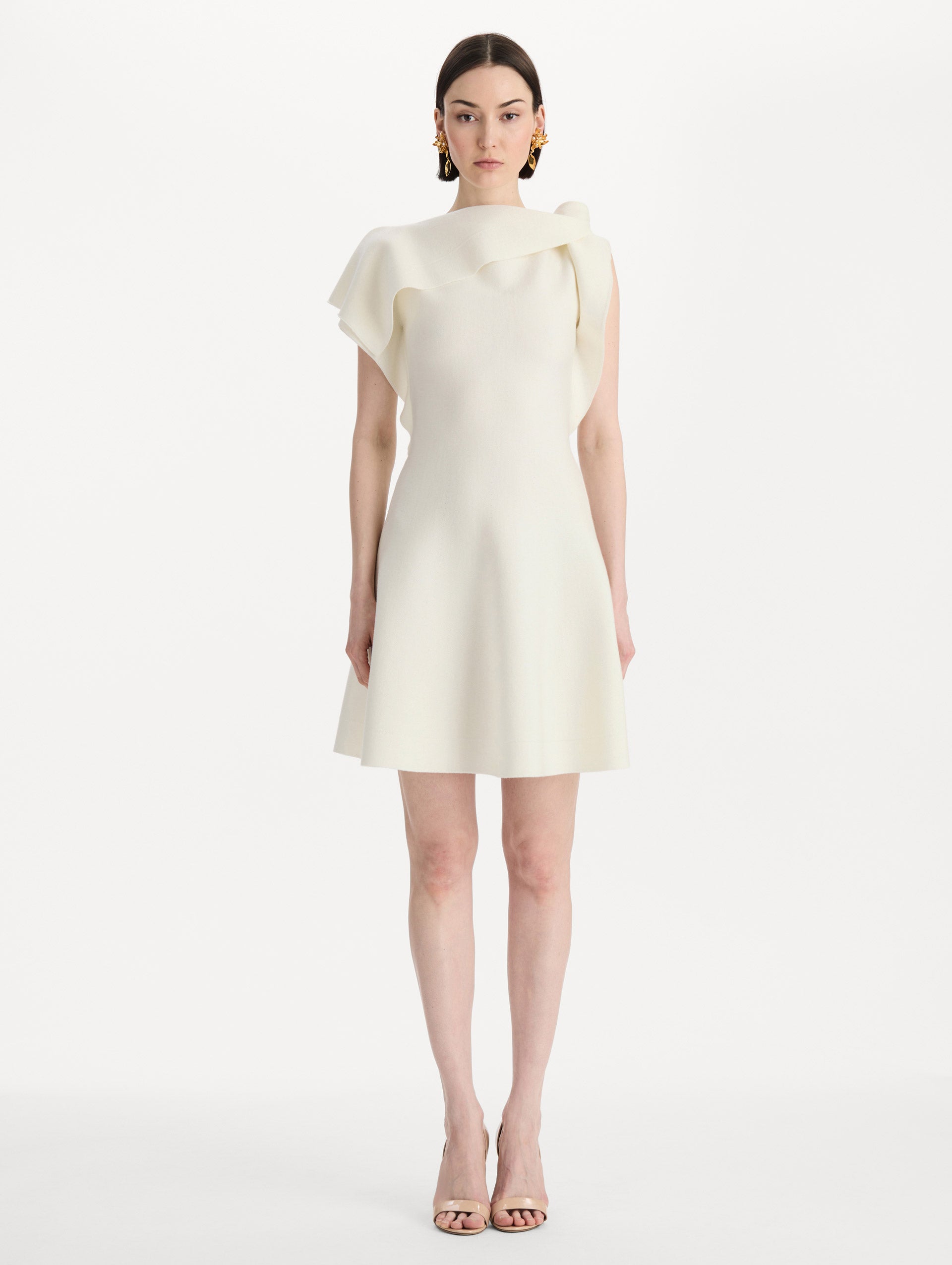 The model is wearing the drape-detailed knit dress with a draped neckline in the color ivory. Front view. 