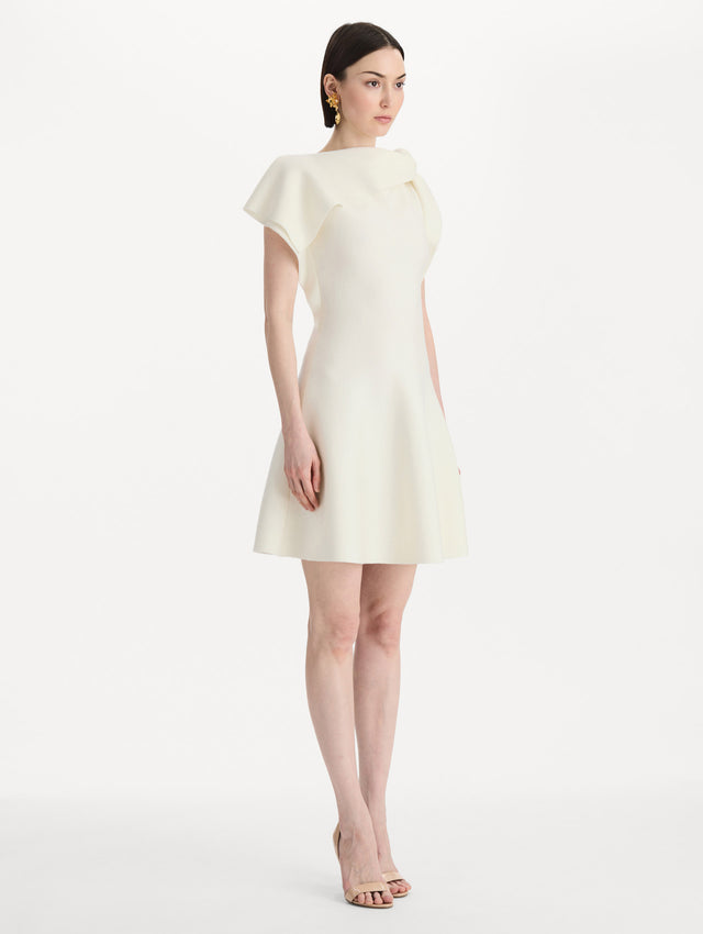The model is wearing the drape-detailed knit dress with a draped neckline in the color ivory. Side view. 