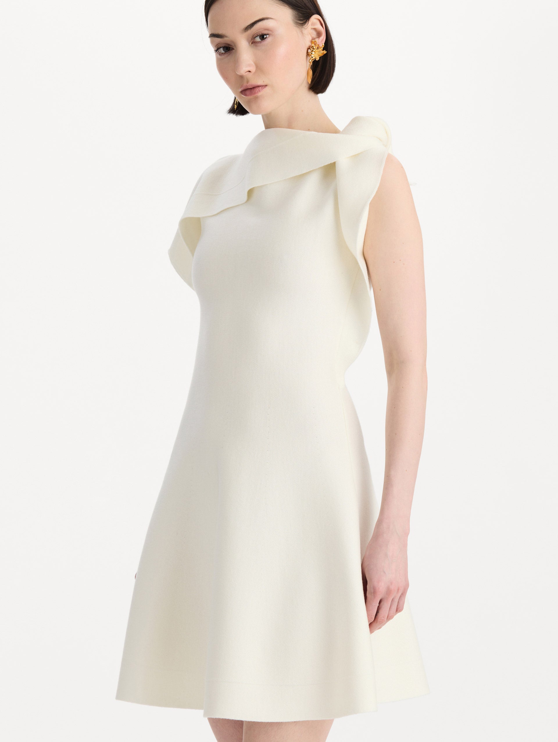 The model is wearing the drape-detailed knit dress with a draped neckline in the color ivory. Zoom view. 