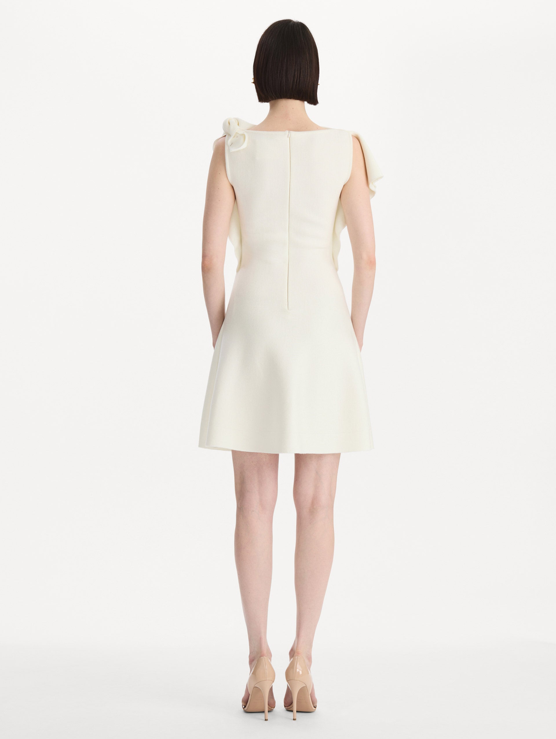 The model is wearing the drape-detailed knit dress with a draped neckline in the color ivory. Back view. 