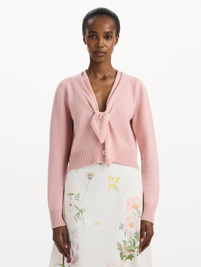 The model is wearing the tie-neck cardigan in blush wool with a tie V-neck detail. Front view.
