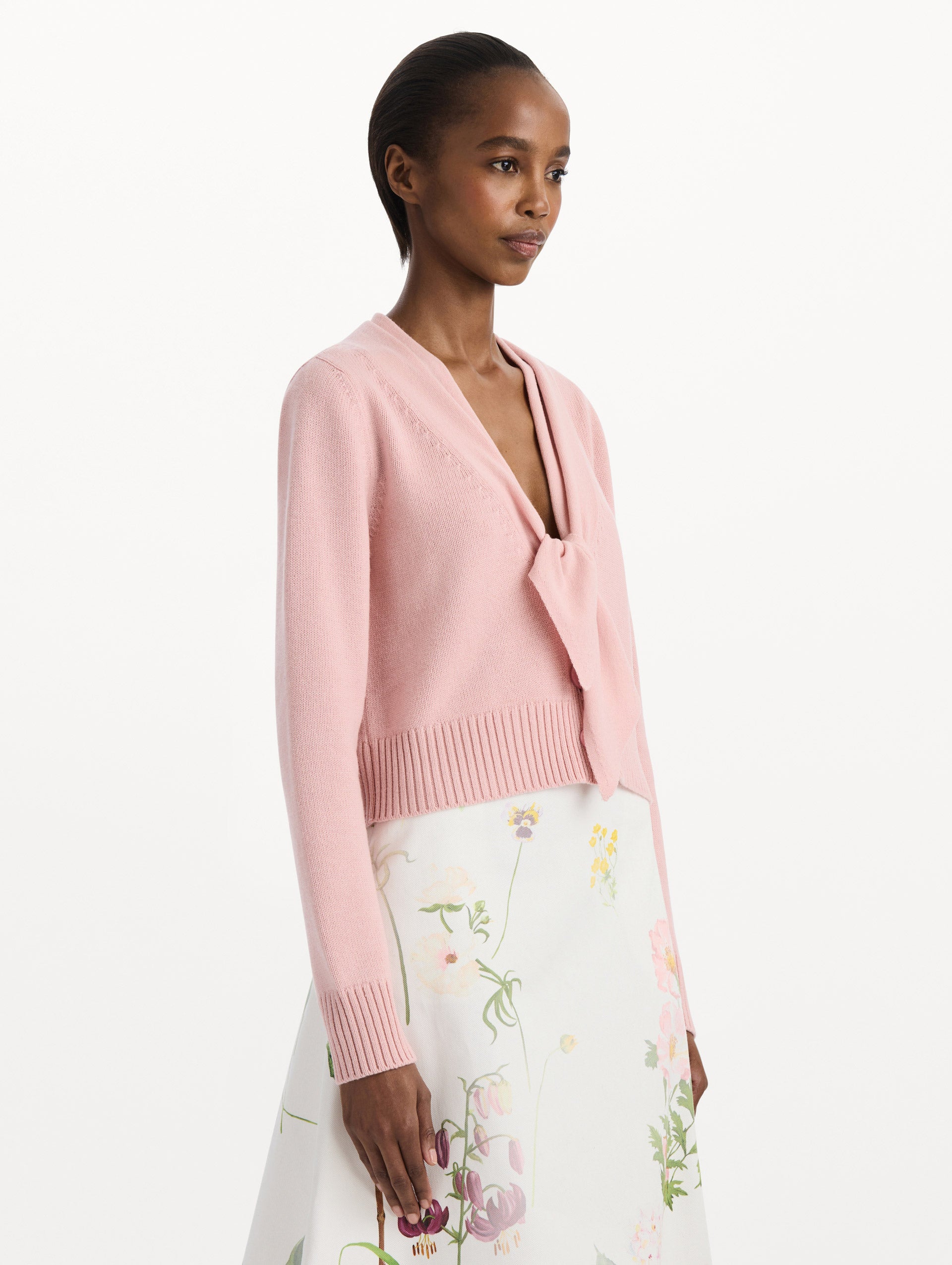 The model is wearing the tie-neck cardigan in blush wool with a tie V-neck detail. Side view.
