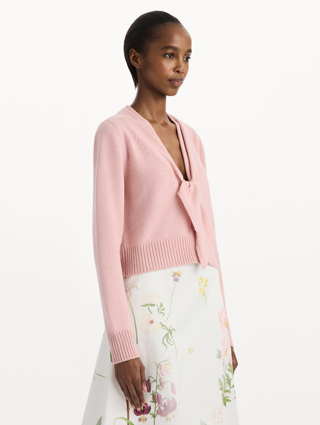 The model is wearing the tie-neck cardigan in blush wool with a tie V-neck detail. Side view.