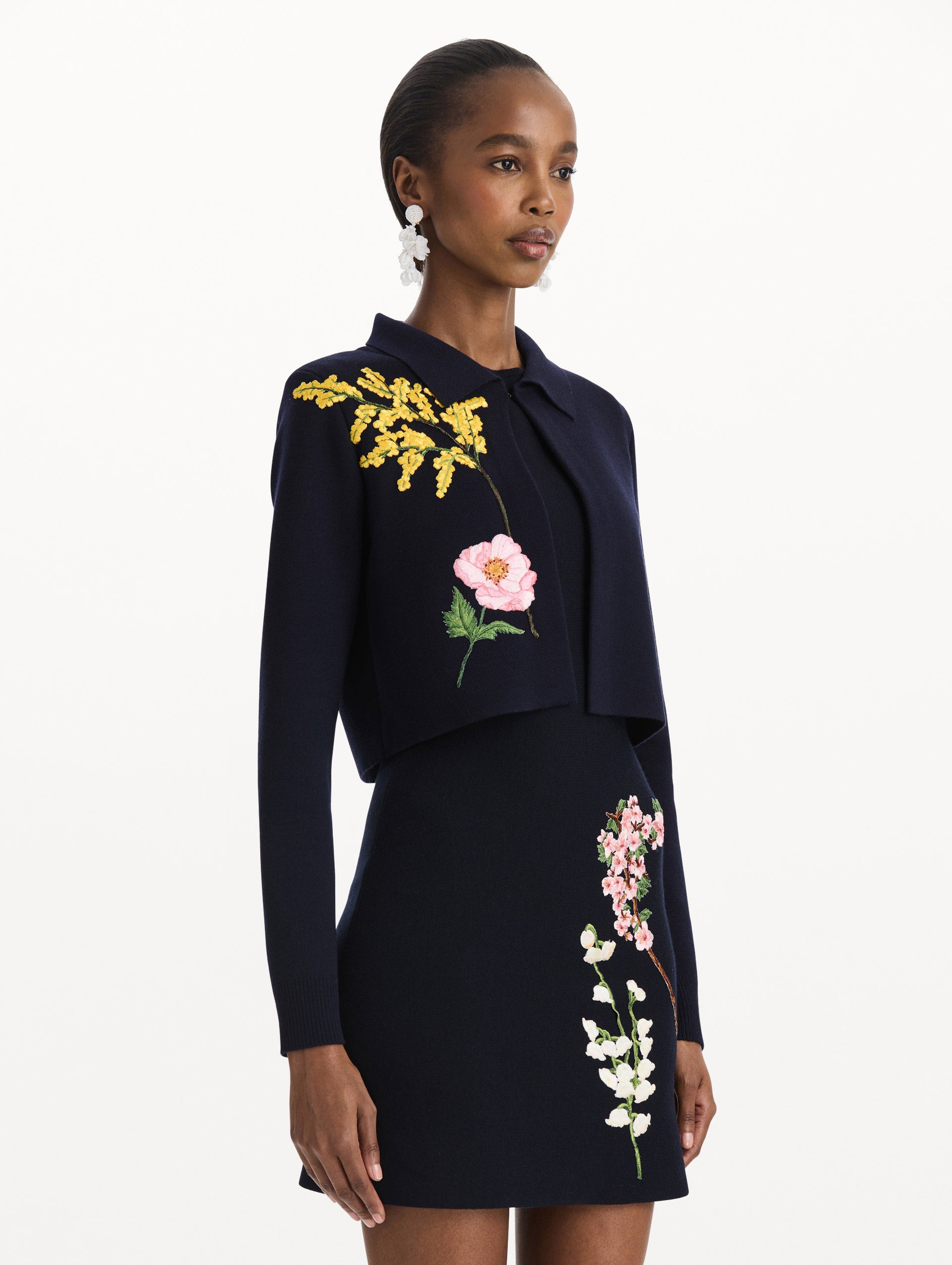 The model is wearing the mixed botanical cropped jacket with delicate embroidery in the color navy. Side view.