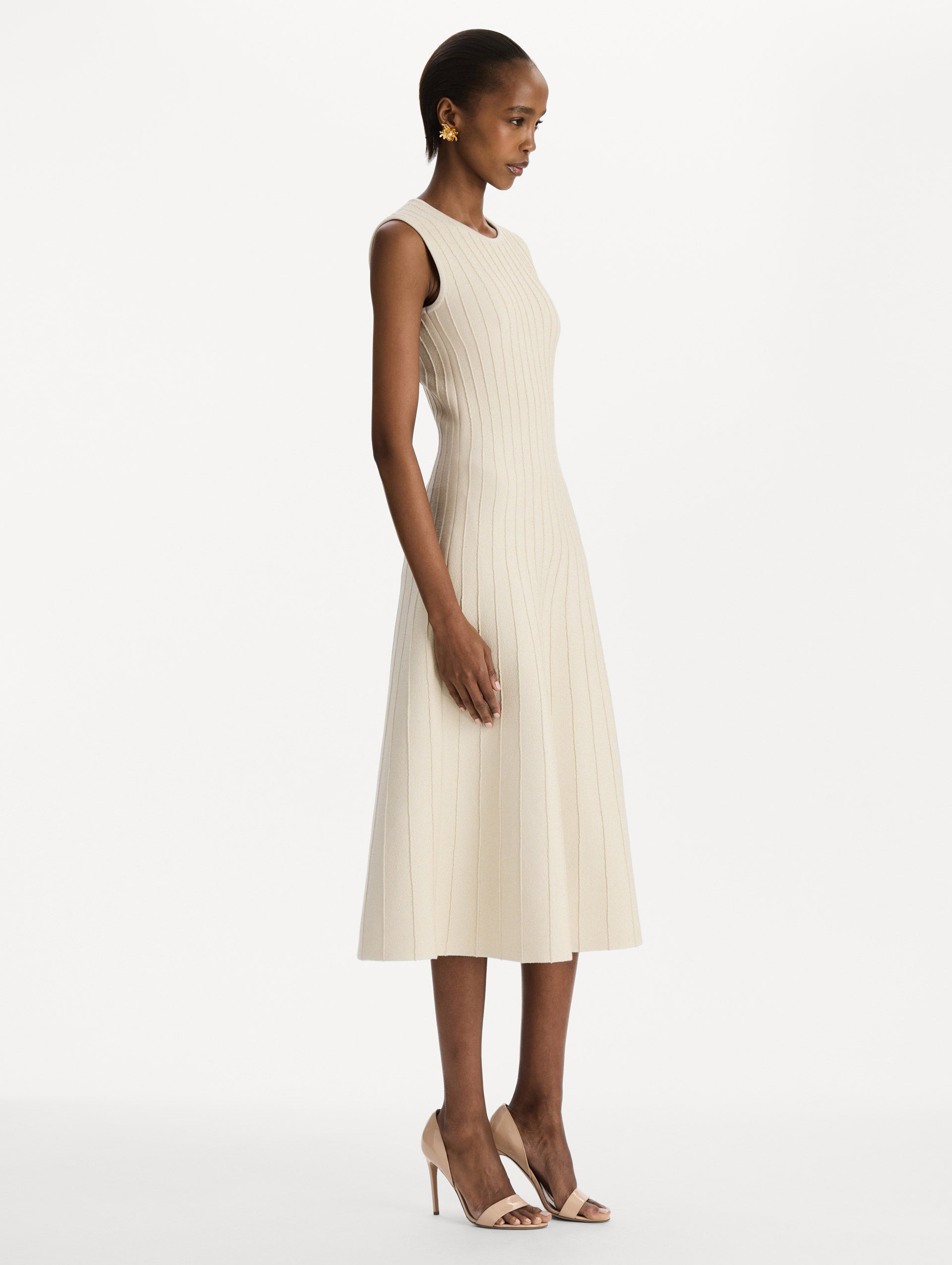 The model is wearing the ottoman knit dress in the color ivory with metallic sparkle yarn detailing. Side view.
