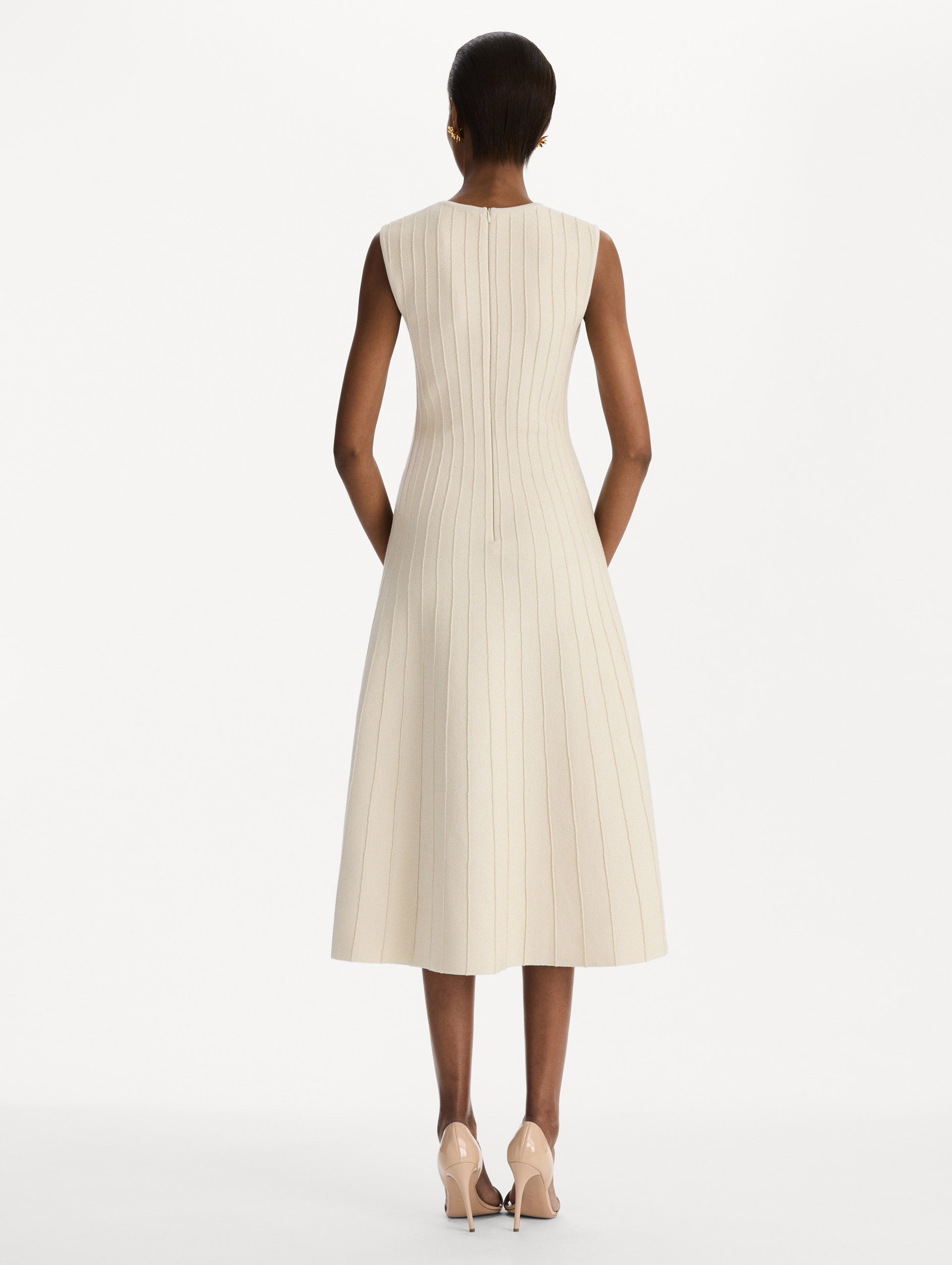 The model is wearing the ottoman knit dress in the color ivory with metallic sparkle yarn detailing. Back view.