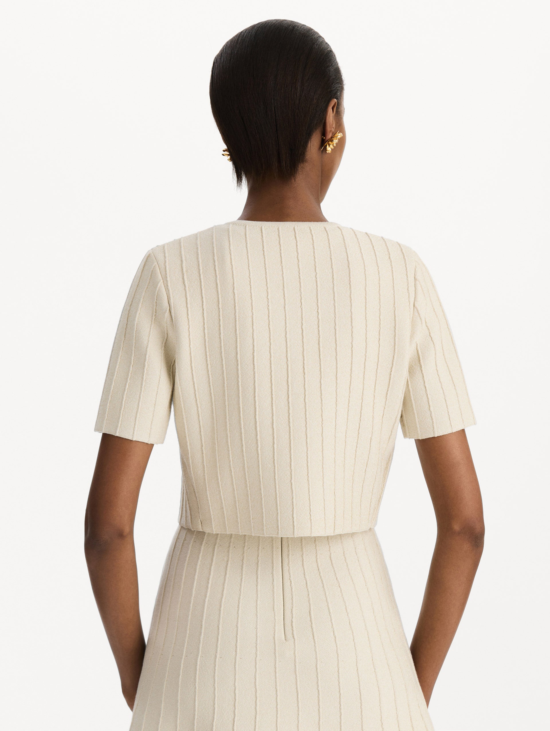 The model is wearing the ottoman cropped cardigan with sparkle yarn detailing in the color ivory. Back view.