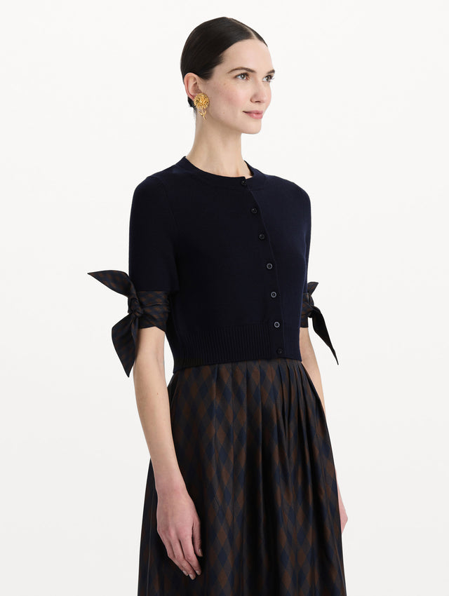 The model is wearing the argyle tie-detailed cardigan in the color navy. Side view. 