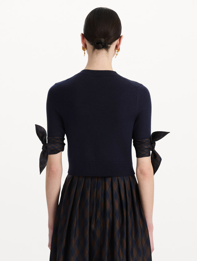 The model is wearing the argyle tie-detailed cardigan in the color navy. Back view. 