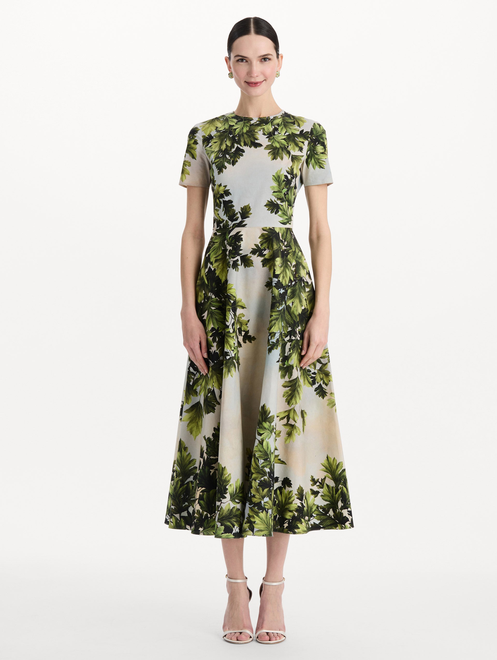The model is wearing the maple leaves cotton poplin dress with short sleeves and an all-over foliage print in the color green multi. Front view. 