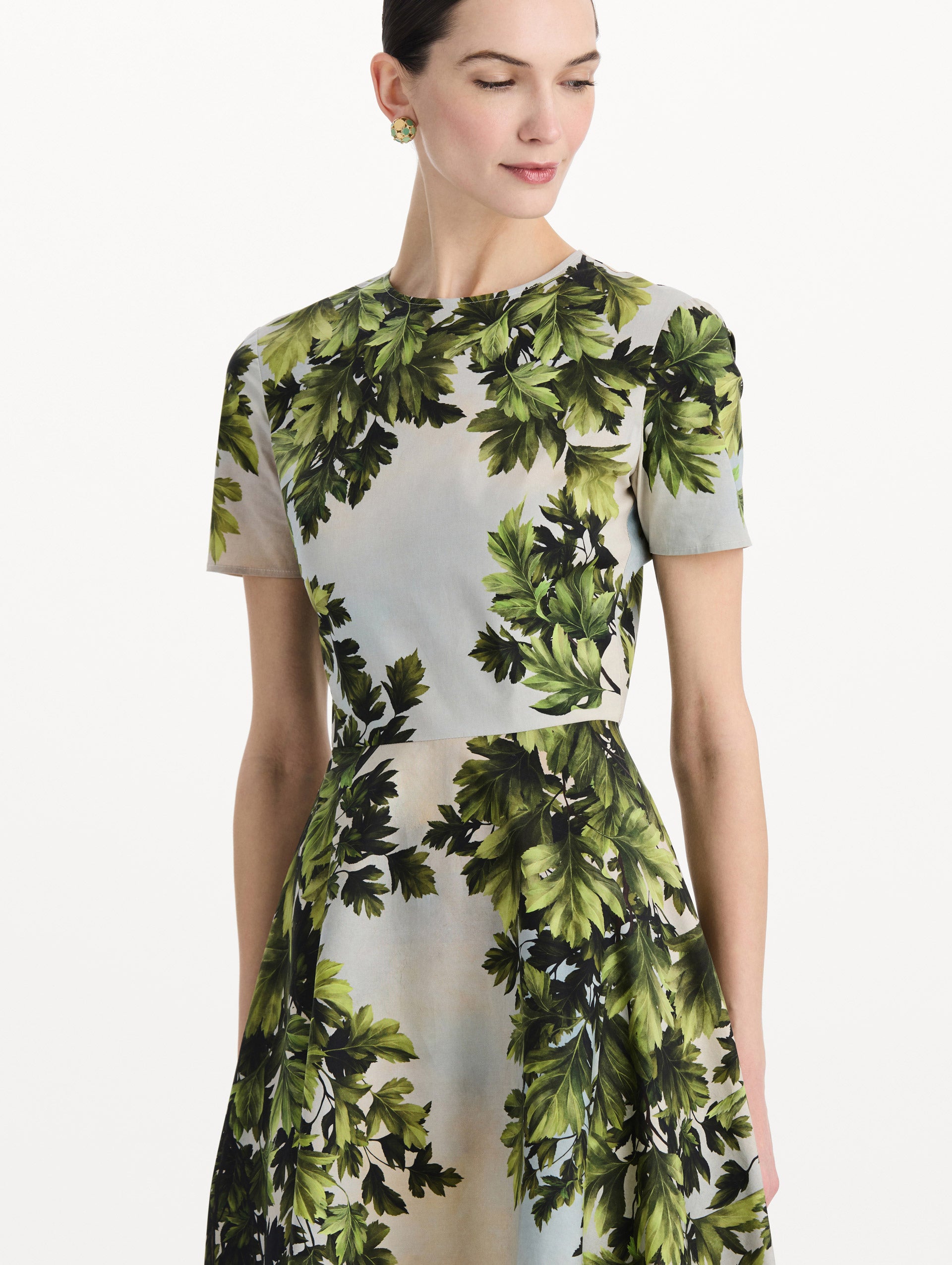 The model is wearing the maple leaves cotton poplin dress with short sleeves and an all-over foliage print in the color green multi. Zoom view. 