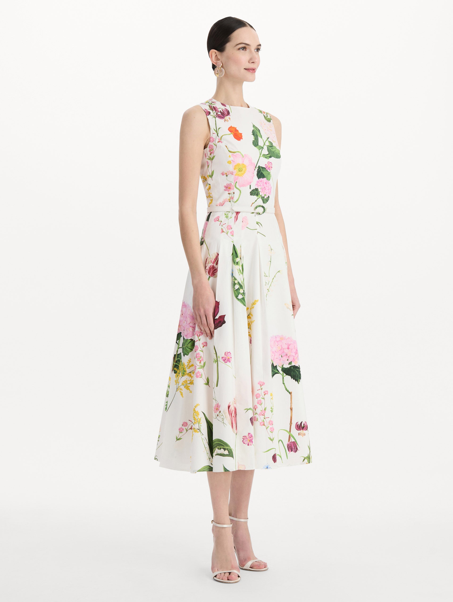 The model is wearing the mixed botanical cotton poplin sleeveless dress with an all-over floral print in white multi. Side view. 