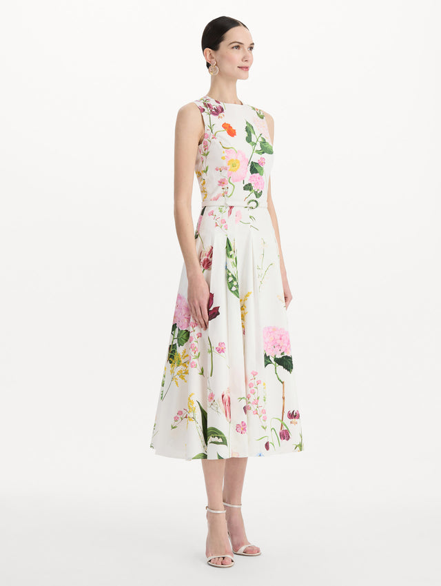 The model is wearing the mixed botanical cotton poplin sleeveless dress with an all-over floral print in white multi. Side view. 