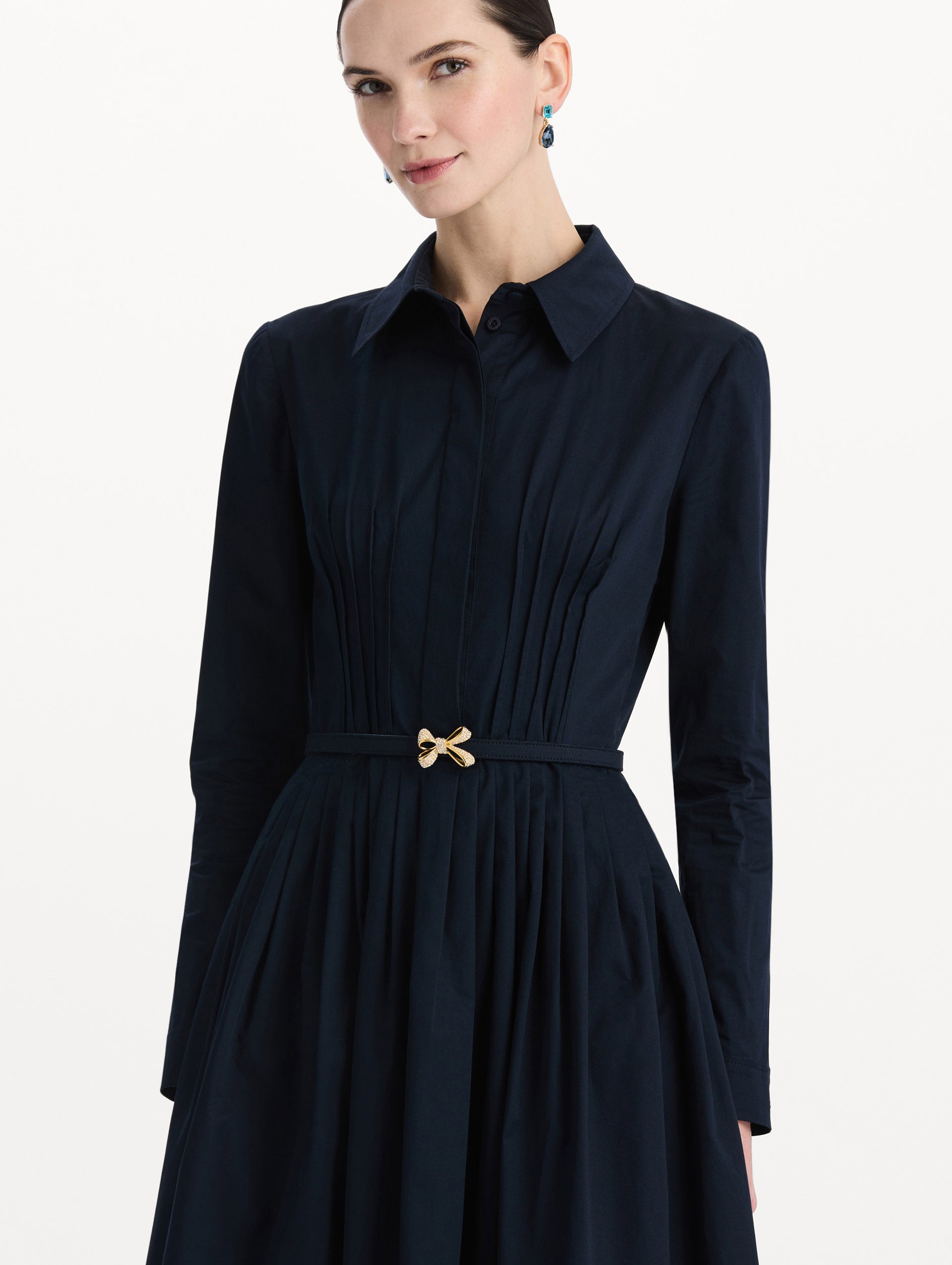 The model is wearing the bow belt cotton stretch twill dress with a collared neckline and long sleeves in the color navy. Zoom view. 