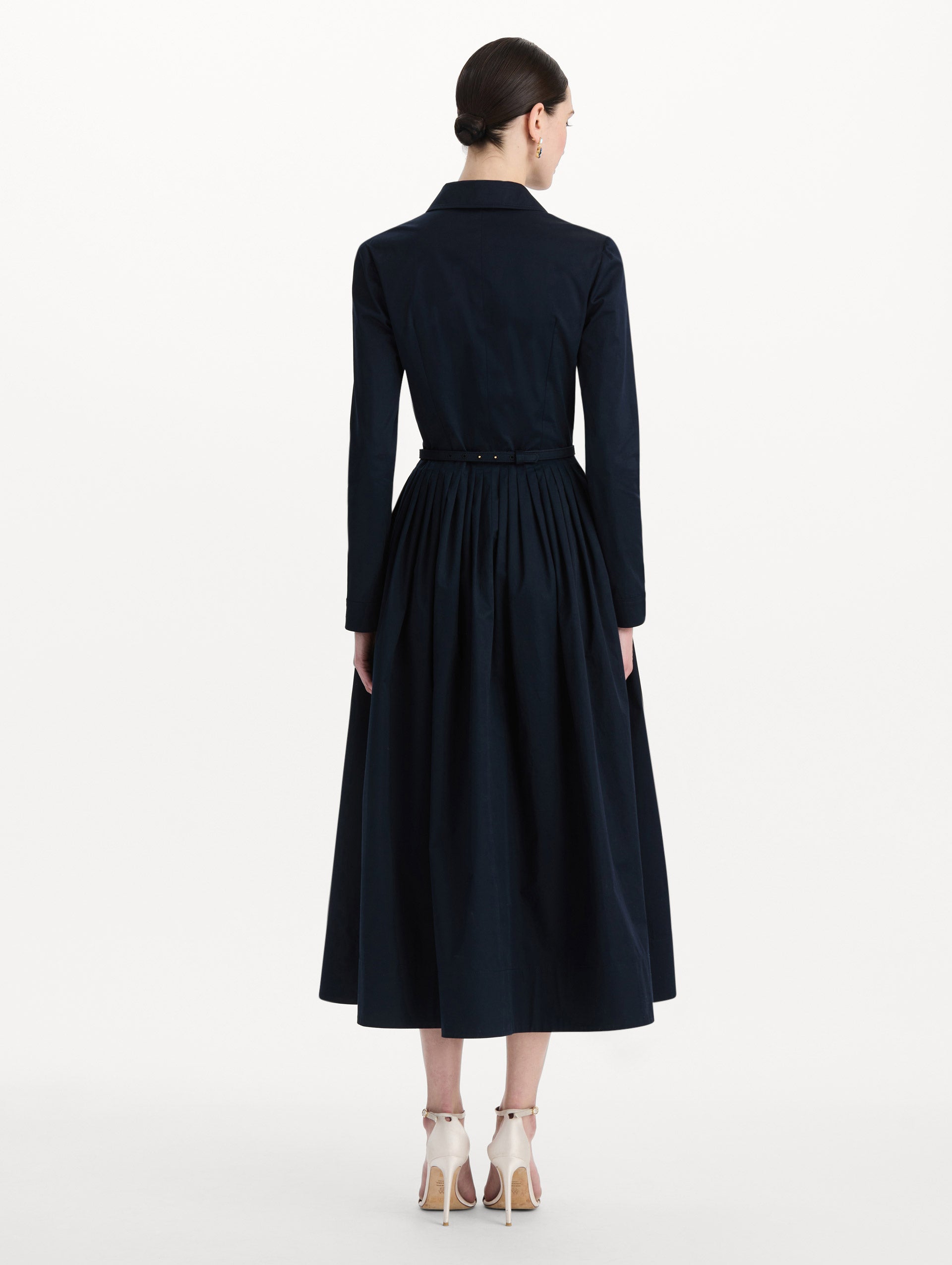 The model is wearing the bow belt cotton stretch twill dress with a collared neckline and long sleeves in the color navy. Back view. 