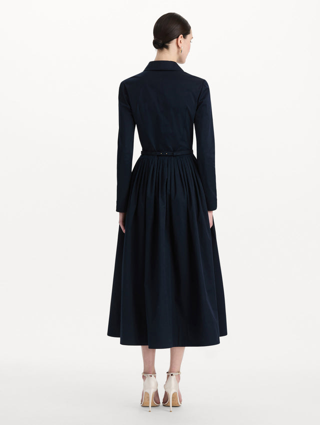 The model is wearing the bow belt cotton stretch twill dress with a collared neckline and long sleeves in the color navy. Back view. 
