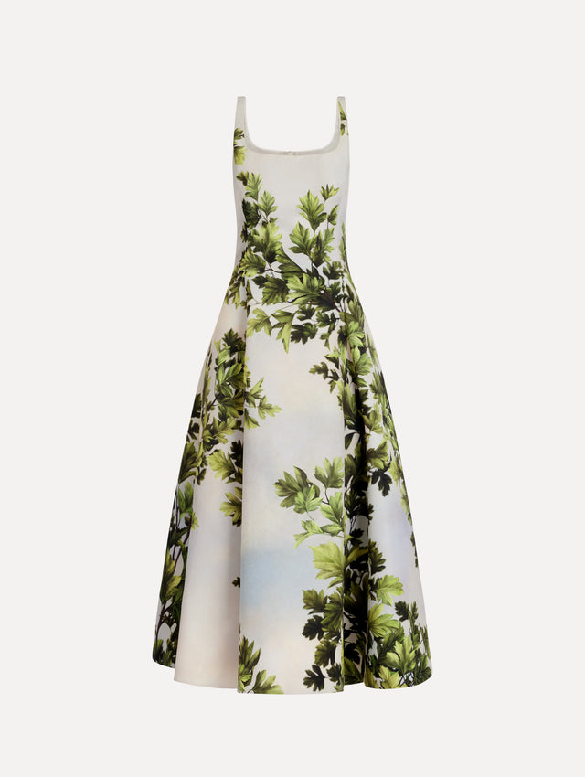 The model is wearing the maple leaves faille dress with a sleeveless scoop neckline and a foliage print in the color green multi.