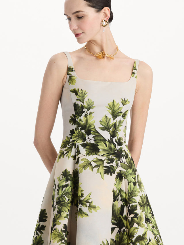 The model is wearing the maple leaves faille dress with a sleeveless scoop neckline and a foliage print in the color green multi. Zoom view. 
