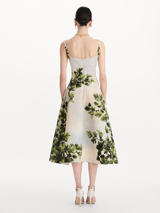 The model is wearing the maple leaves faille dress with a sleeveless scoop neckline and a foliage print in the color green multi. Back view. 
