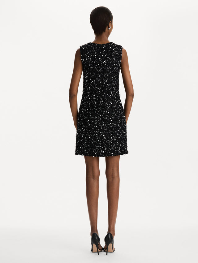 The model is wearing the sequin ribbon tweed sleeveless day dress in black and white. Back view. 