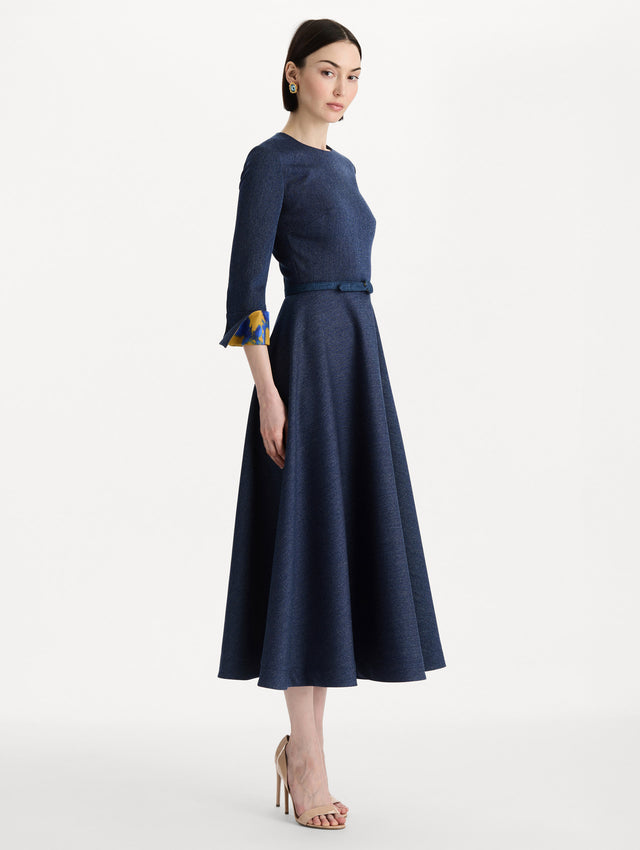 The model is wearing the peony cuff wool dress in the color indigo with peony-print cuffs and midi sleeves. Side view. 